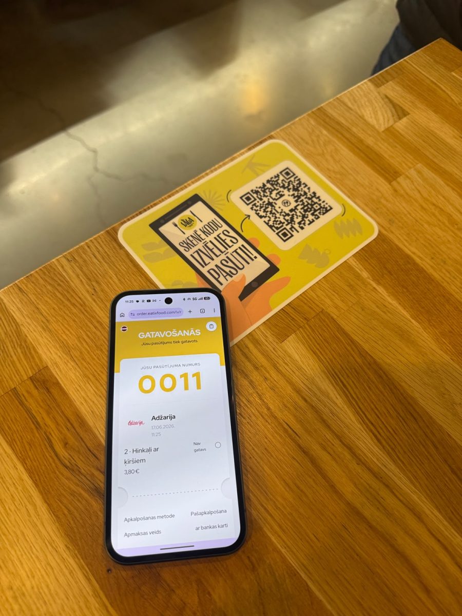A guest's phone showing an Eatix order being prepared at Adžarija, next to the SĀGA table QR code card